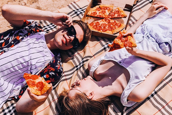 Stylish couple eating pizza at the beach